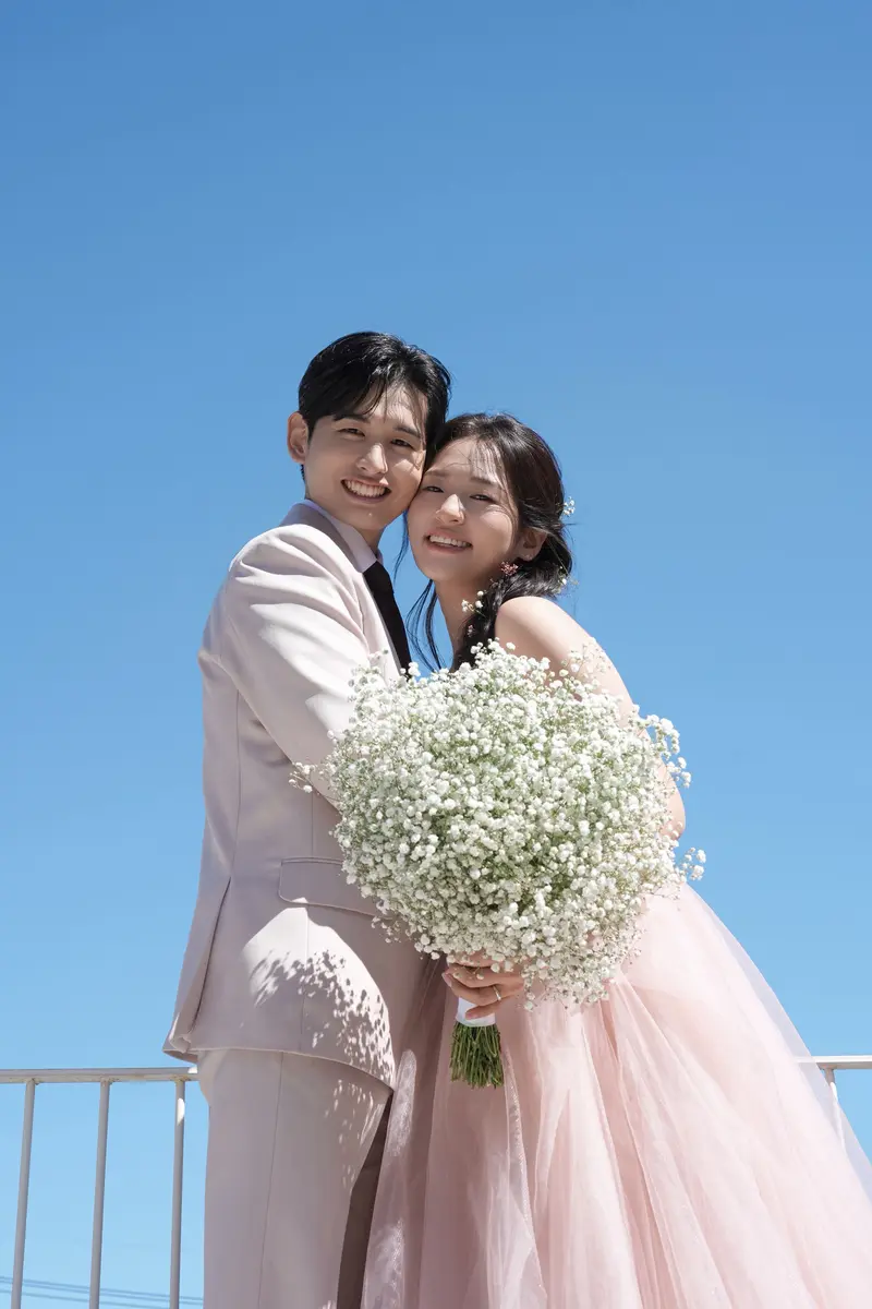 푸른 하늘 아래 볼을 맞대고 웃는 두 사람. 신부가 안개꽃 부케를 들었다